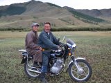 Dwóch Mongołów jadących motocyklem po stepie z górzystym krajobrazem w tle, nowoczesny środek transportu w tradycyjnym otoczeniu. #22