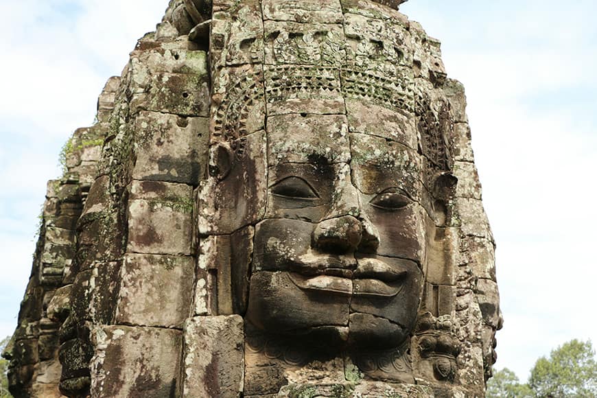Zbliżenie na uśmiechniętą kamienną twarz wieży świątyni Bayon, stanowiącej część Angkor Thom, dawnej stolicy imperium Khmerów.